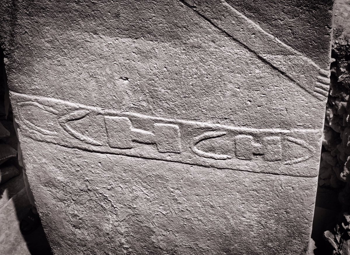 Close view of a carved belt with H- and C-shaped symbols on a central pillar