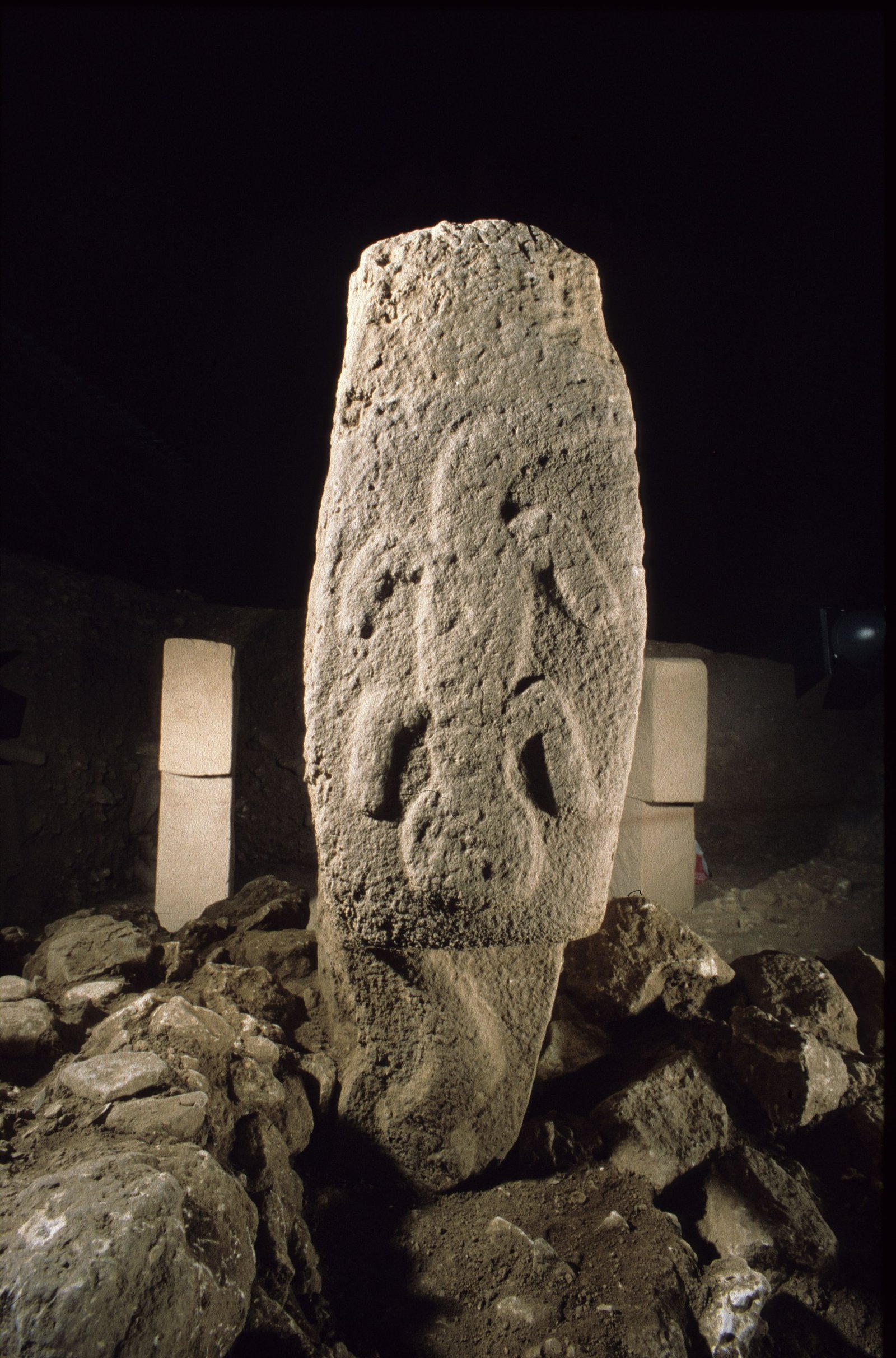 A carved standing pillar of Enclosure B lit at night among other pillars of the ring