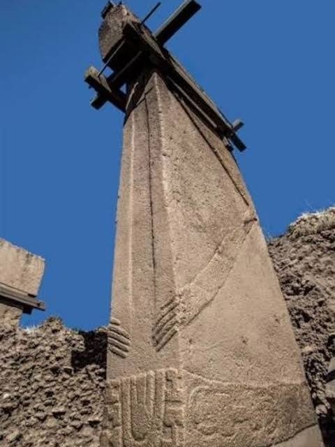 Central Pillar 18 of Enclosure D shot from below against the sky — a carved arm and long-fingered hand curving to the waist above a belt and fox-pelt loincloth