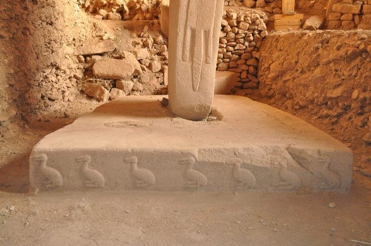 The base of central Pillar 18 rising from its pedestal, with a row of carved ducks running along the front of the platform