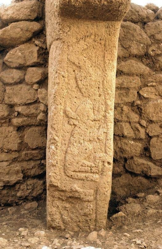 Ring-wall Pillar 20 of Enclosure D against a dry-stone wall, its shaft carved with a vertical sequence of animal reliefs
