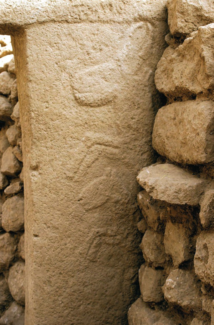 Ring-wall Pillar 21 of Enclosure D against a dry-stone wall, with faint, worn animal reliefs on the shaft