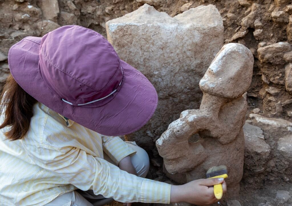 The statue being cleaned after lifting — the human figure and the leopard beneath it emerging as the soil is removed.