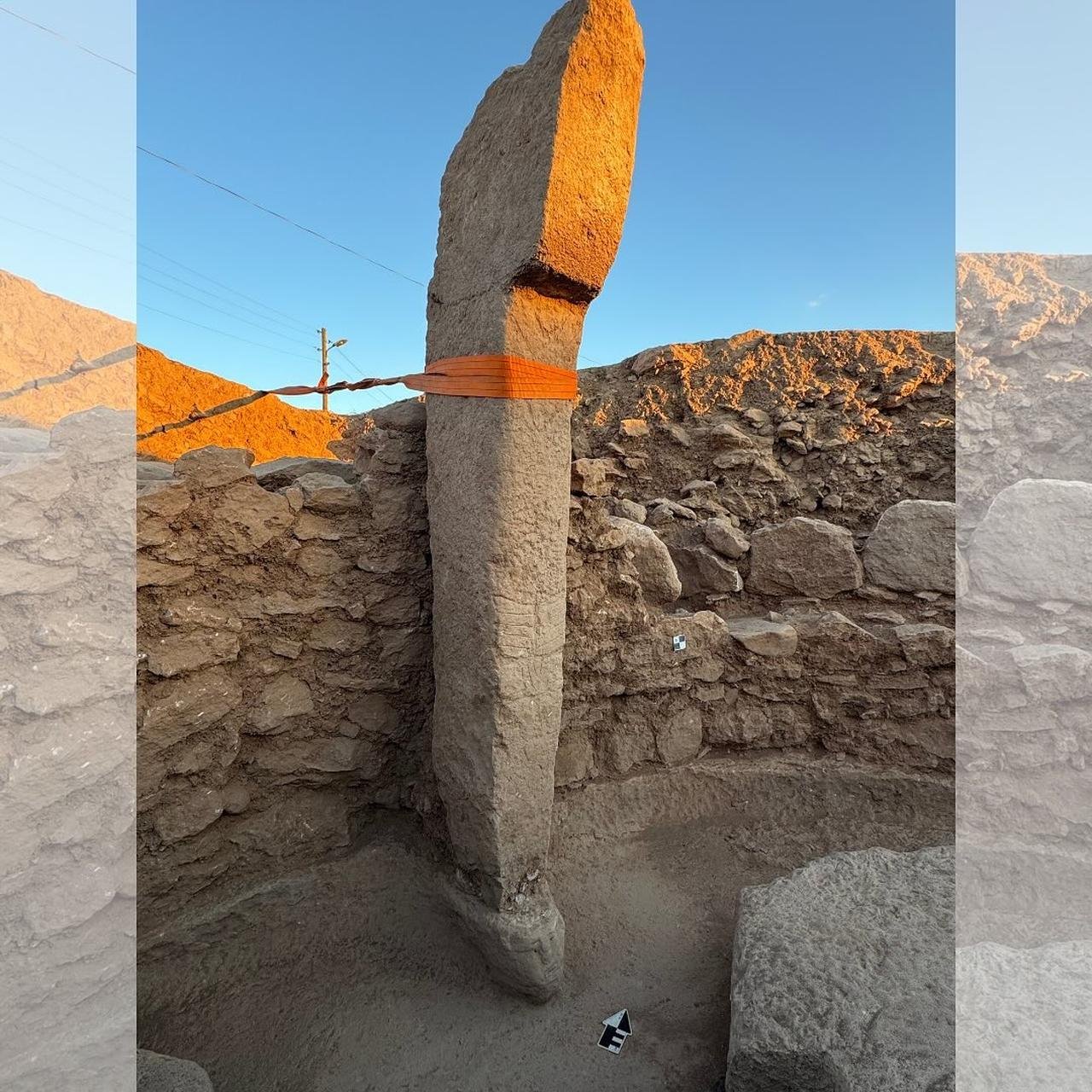 A tall upright Neolithic pillar strapped for preservation, standing in an excavated stone-walled room at Sayburç