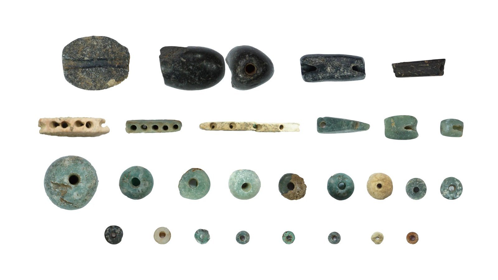 Dozens of small stone beads, rings and worked-stone objects of varied colours arranged on a dark background